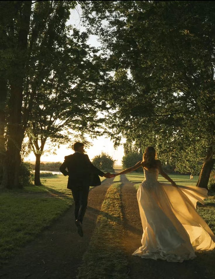 A couple running hand in hand down a tree-lined path at sunset.