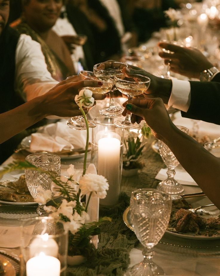 Guests raising glasses of champagne over a candlelit dinner table.