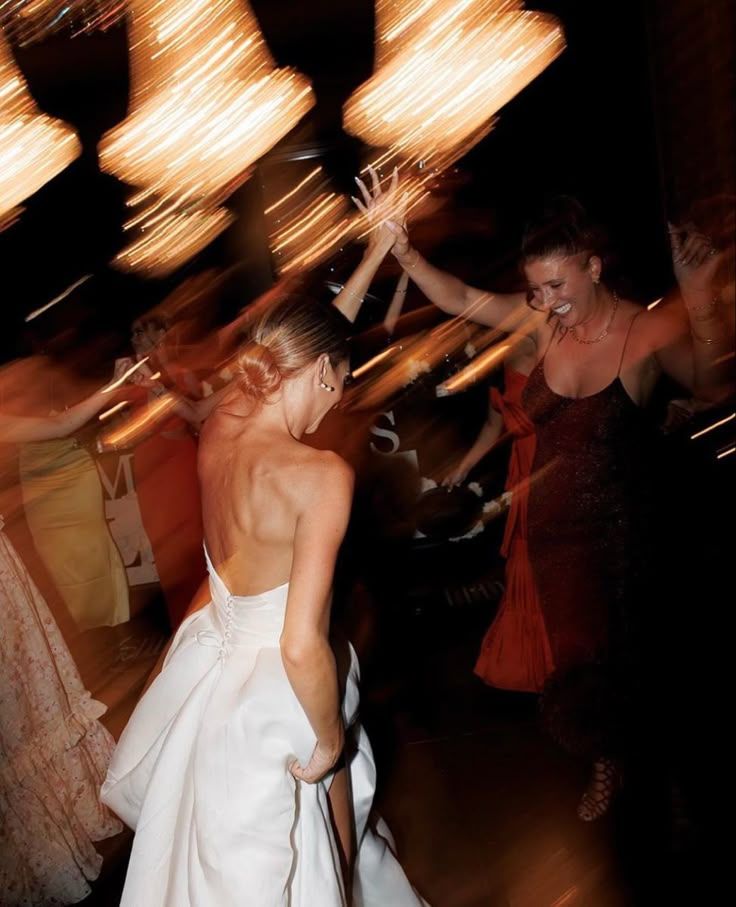 The bride dancing with friends under warm, blurred lights at the evening party.