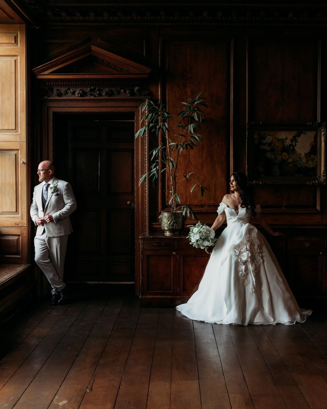 A bride and groom in a wood-panelled Georgian room, light falling through a tall window.